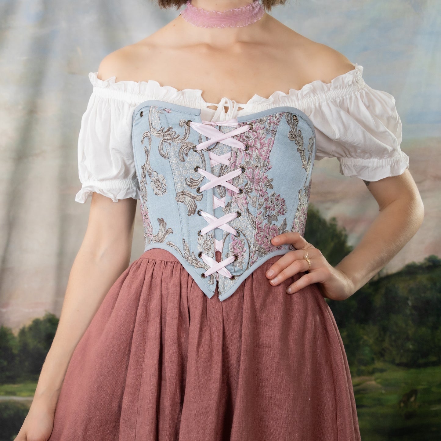 model wearing a renaissance costume with a blue corset and a pink skirt with matching pink ribbons