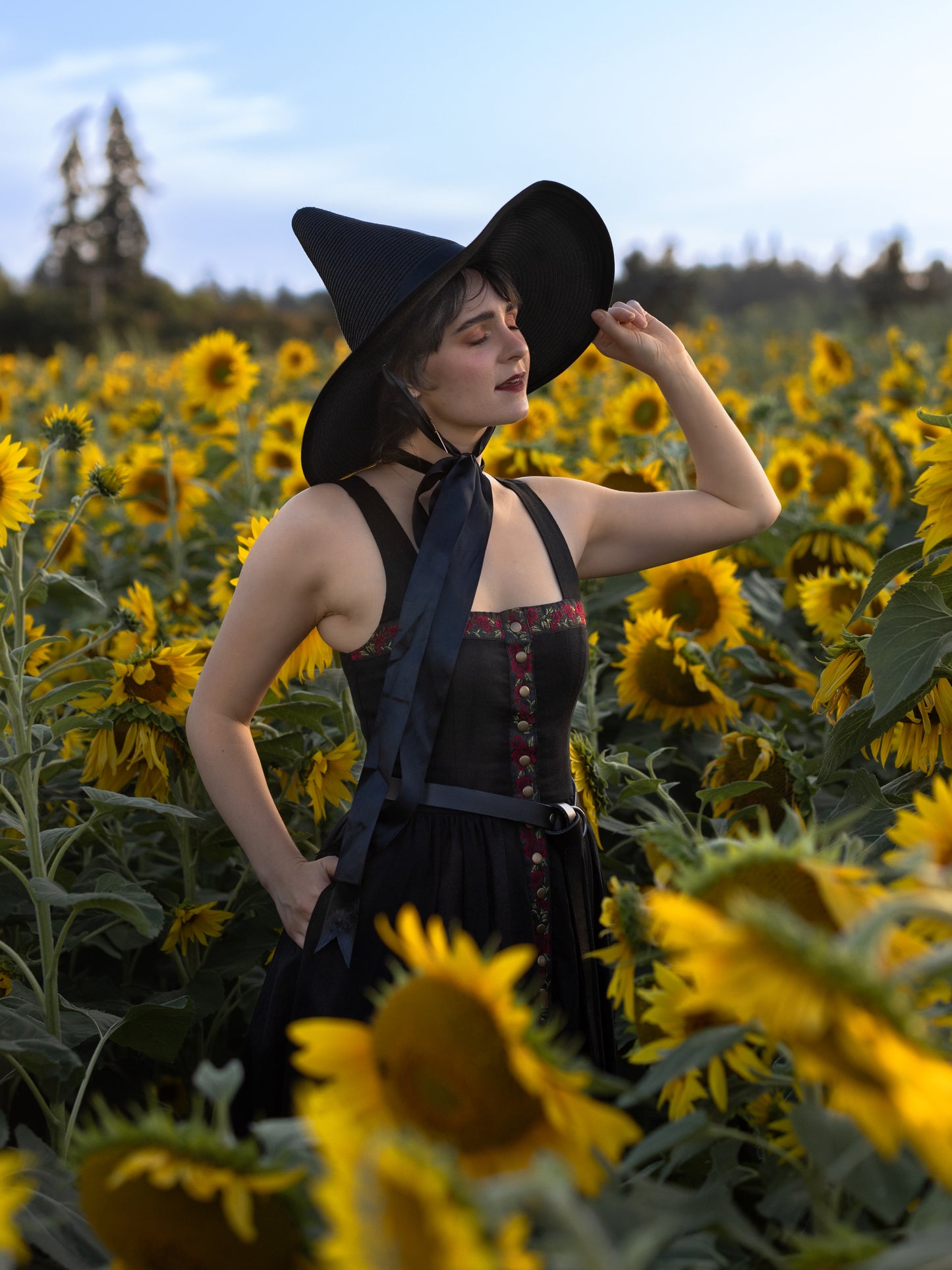 model wearing witch hat and black witchy dress, tilting her hat up to let some sun on her face